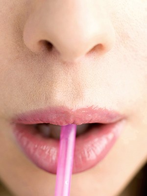 The face of a woman blowing on a pink straw