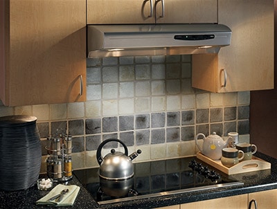 Kitchen shot of the Broan under cabinet range hood, silver in color. It's installed under two cubboards above an electric stove.